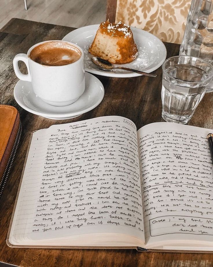 an open book sitting on top of a wooden table next to a cup of coffee