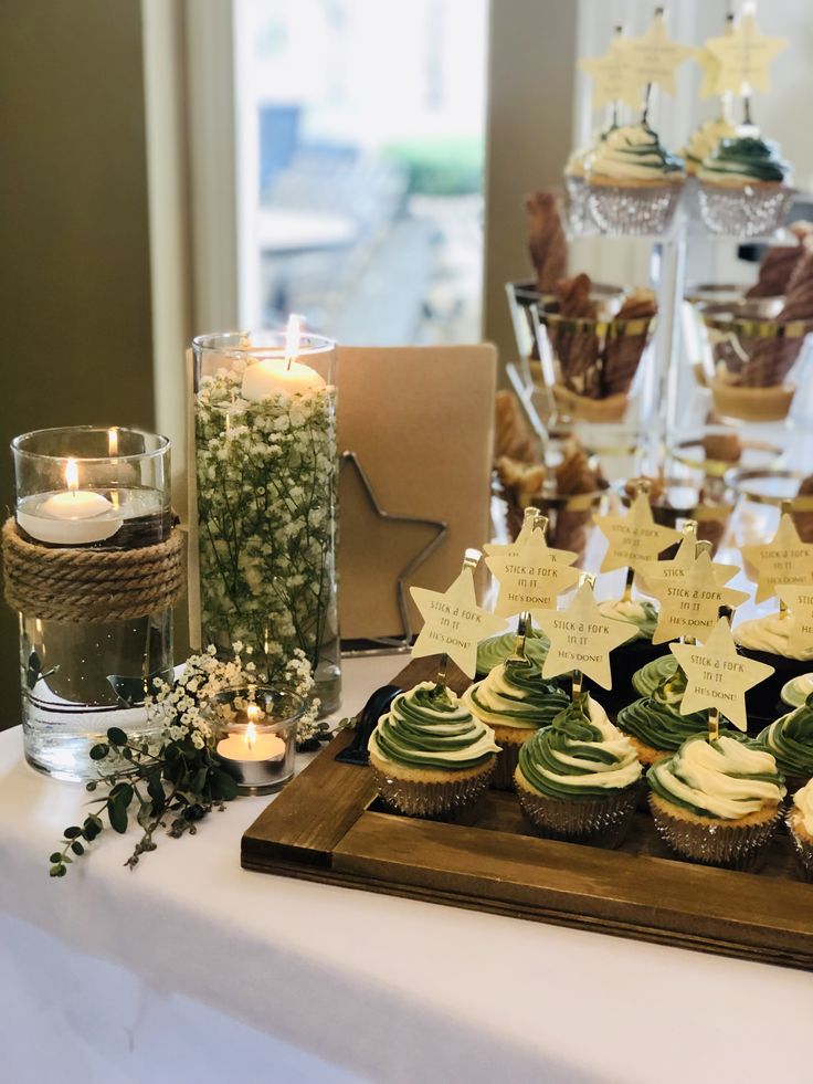 cupcakes are arranged on a wooden tray near candles and other decorations at a wedding reception