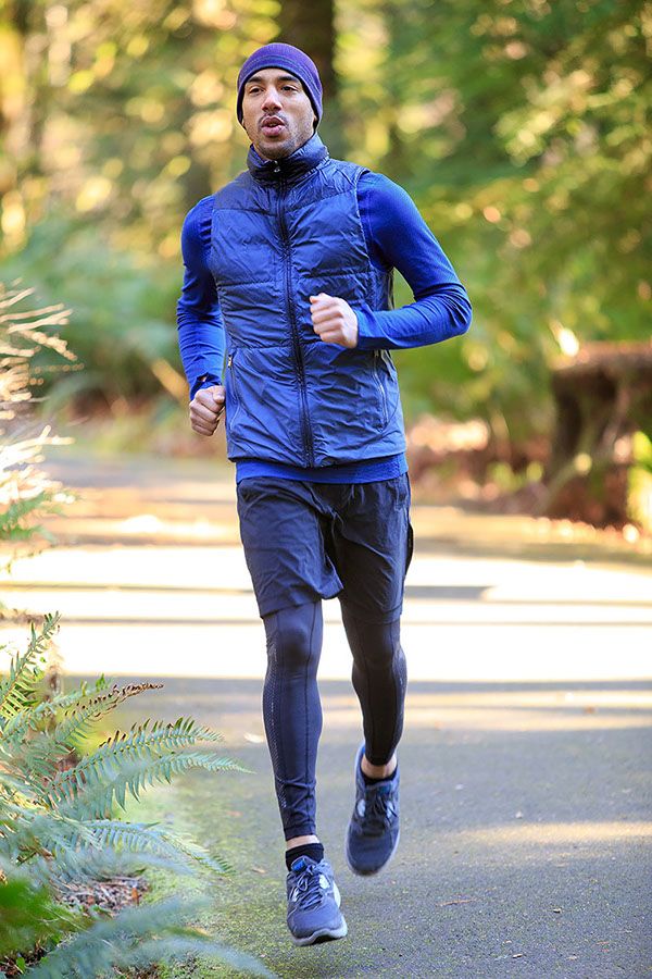 a man running down a path in the woods wearing a blue jacket and hat with his mouth open