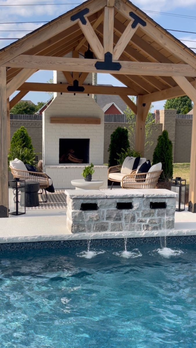 an outdoor living area next to a pool with a fire place and grill in the middle