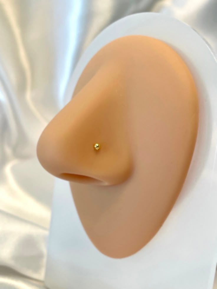 a close up of a plastic head on a white base with a gold nose ring