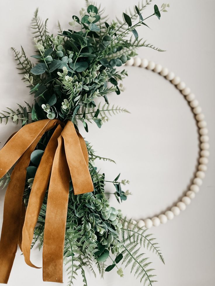 a wreath with greenery and ribbon hanging on the wall next to a pearl necklace