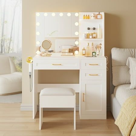 a white vanity with lights on it next to a bed and chair in a room