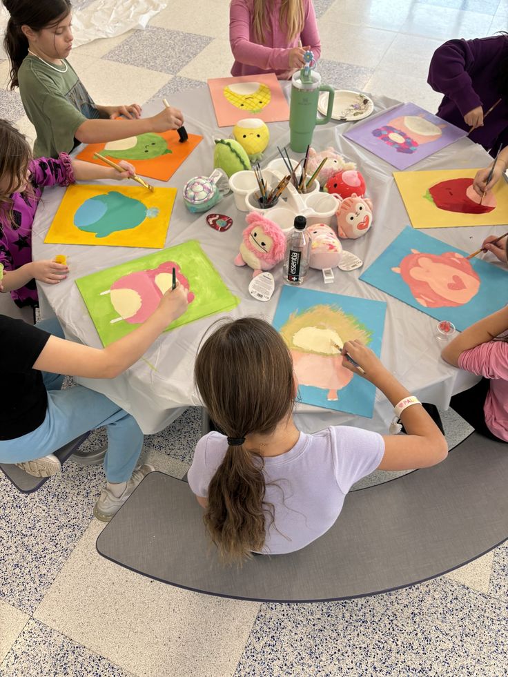 a group of children sitting around a table with paintings on it