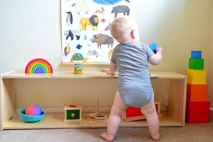 a baby standing in front of a wooden shelf with toys on it's sides