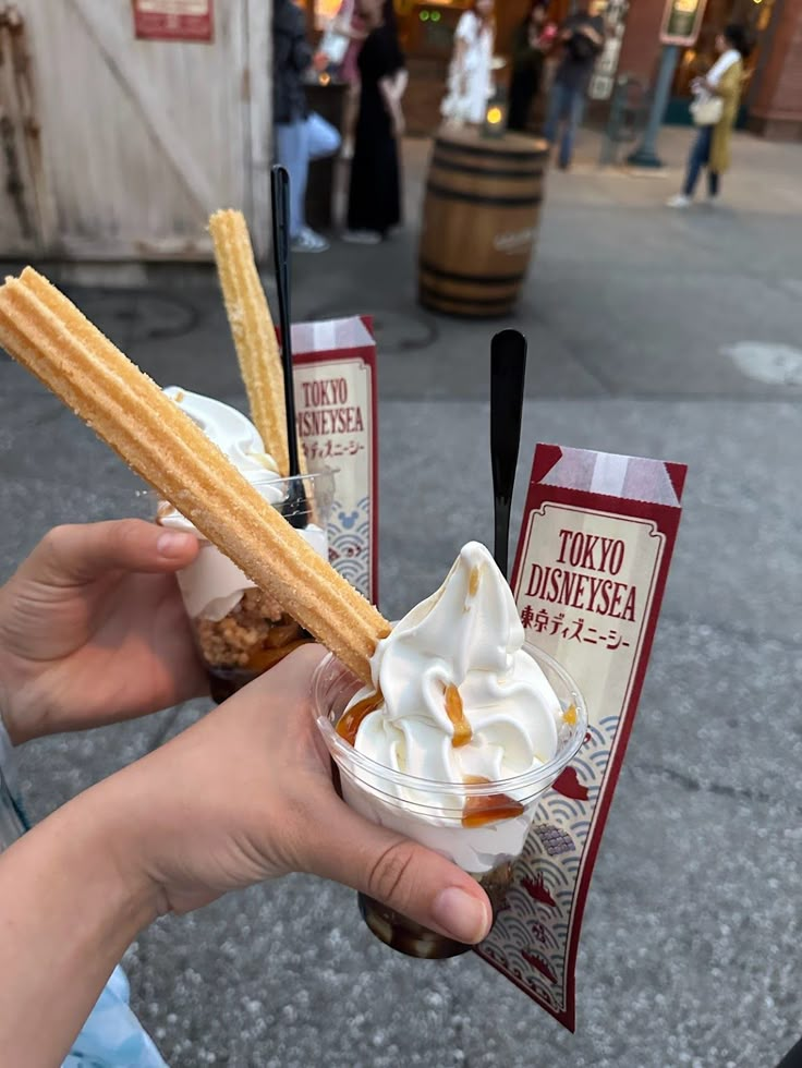 a person holding two ice cream sundaes with waffle sticks sticking out of them