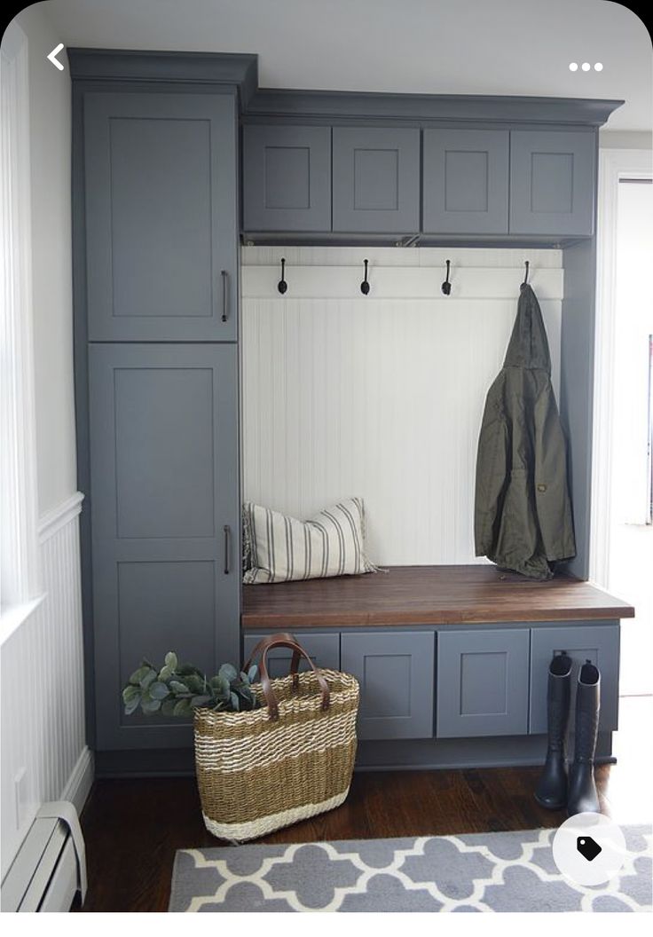 a bench and coat rack in a room with wooden floors, white walls and gray cabinets