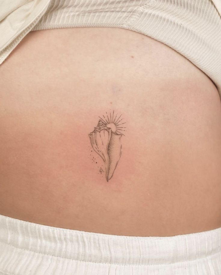 the back of a woman's stomach with a shell tattoo on her left side