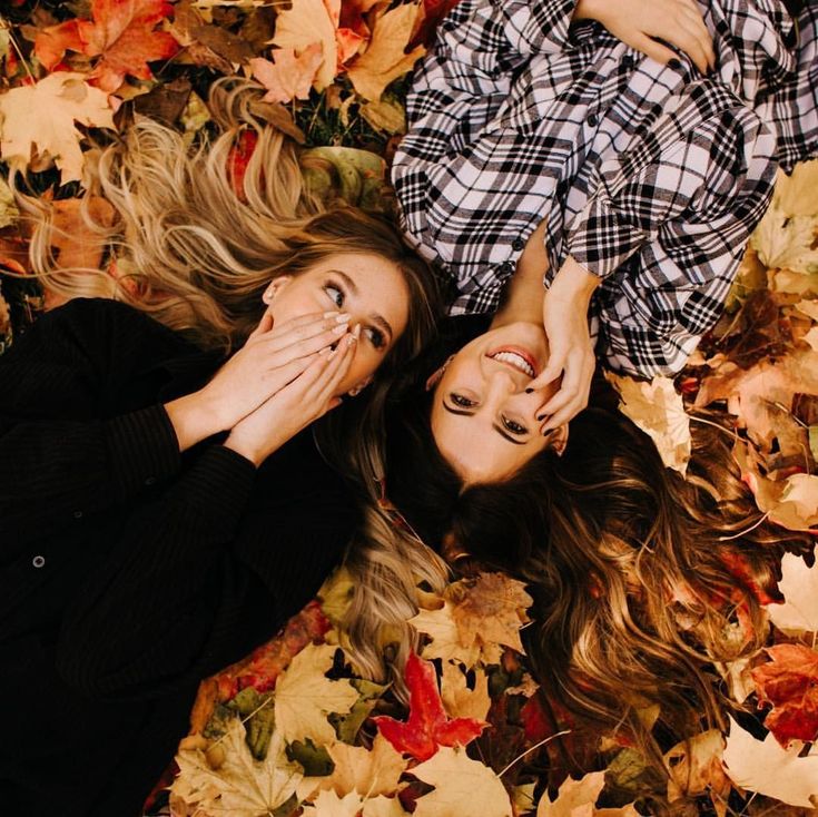 two women laying on the ground covered in leaves with their hands over their mouths and looking at the camera