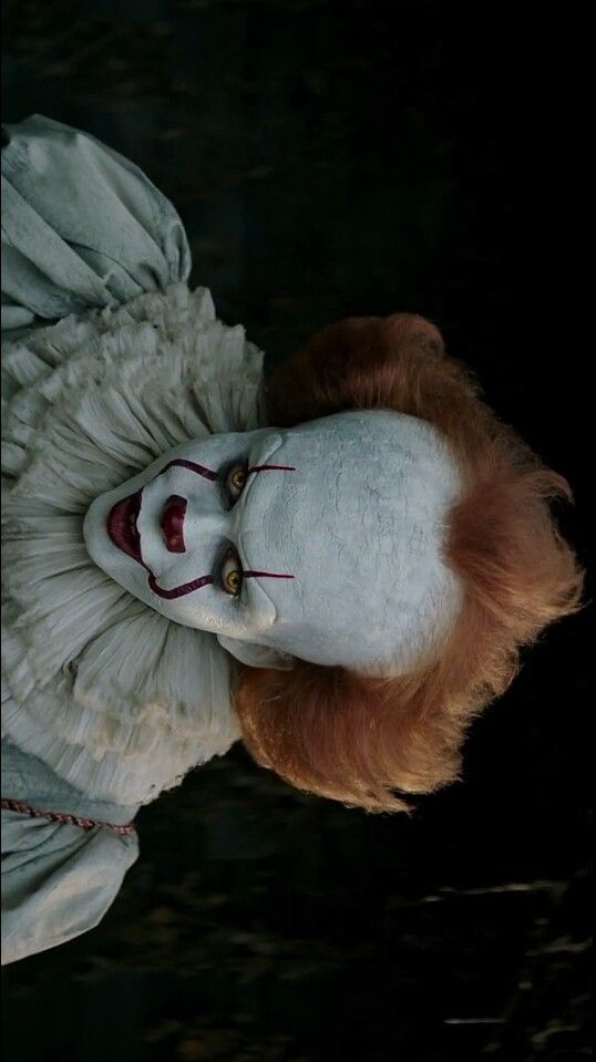 a creepy clown with red hair and white makeup is looking at the camera from above