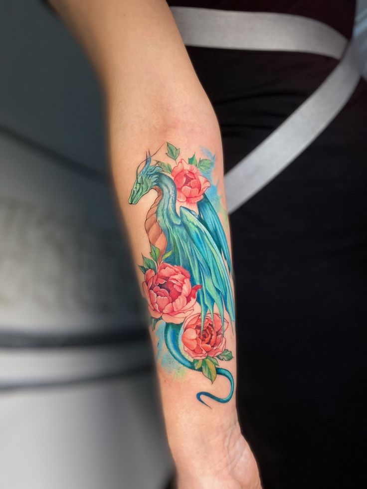 a woman's arm with a dragon and roses tattoo on the left side of her arm