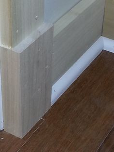 the corner of a room with wood flooring and white paint on it's walls