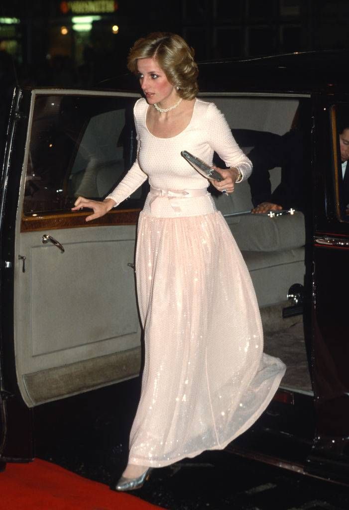 a woman in a long white dress stepping out of a car with her hand on the door handle