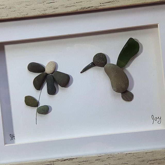 two pebbles are placed in a white frame and one is holding a flower