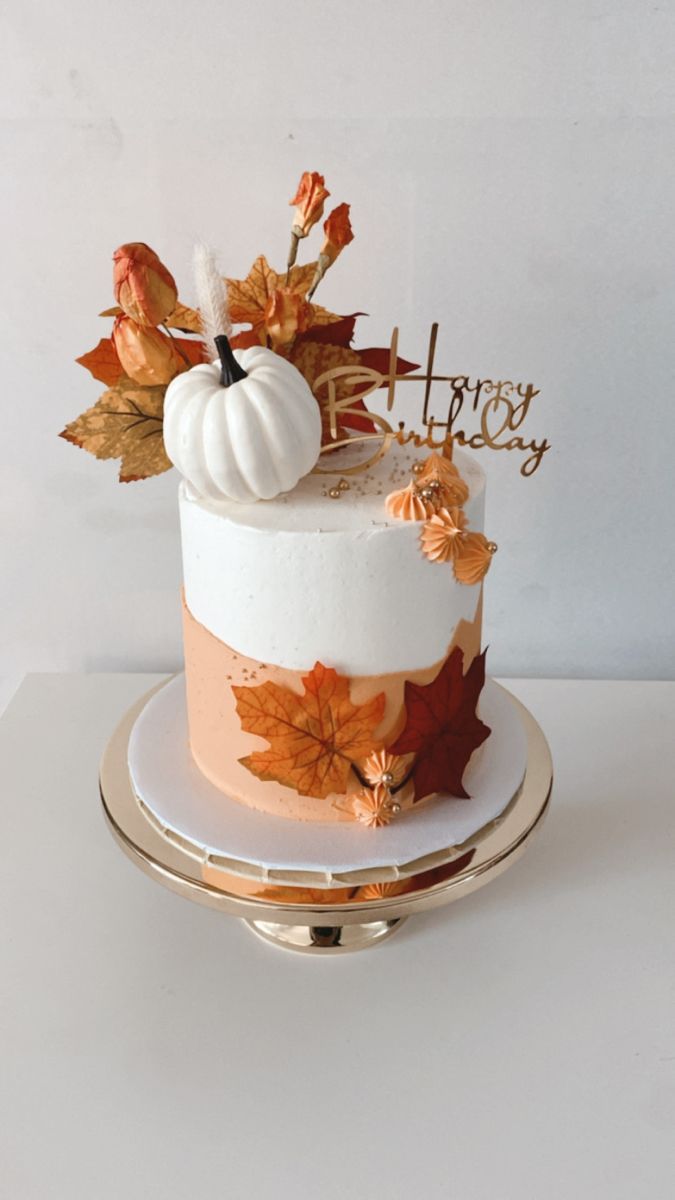 a white and orange cake with fall leaves on the top is sitting on a gold plate