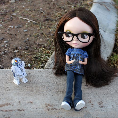 a doll with glasses sitting next to a toy r2d2 robot on the ground