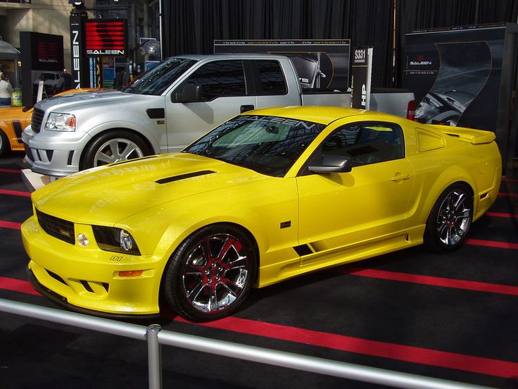 a yellow sports car parked in front of other cars on display at an auto show