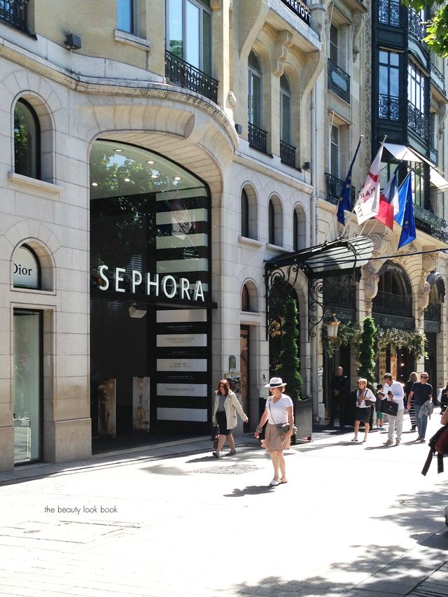 people are walking on the sidewalk in front of sephora store, with flags flying overhead