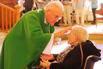 an old man in a wheelchair getting his hair combed by another older gentleman who is wearing a green robe