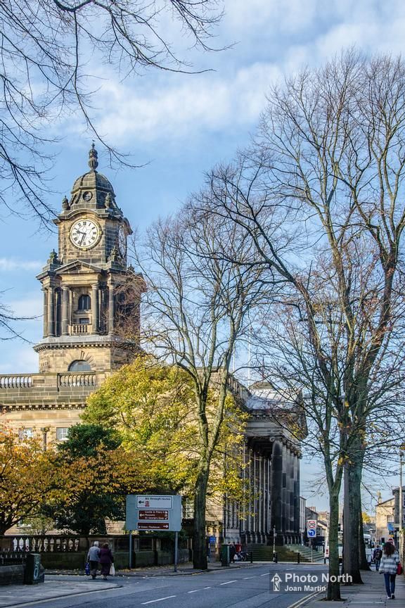 a clock tower on top of a building with trees in the foreground and people walking by