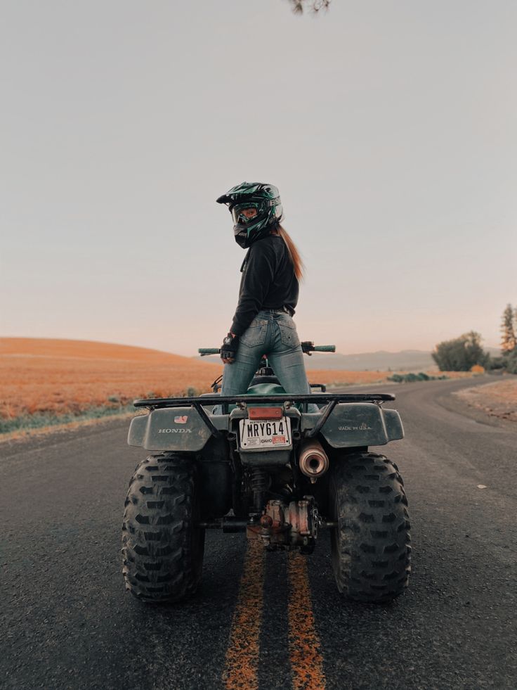 a person riding on the back of an atv in the middle of a road with grass and trees