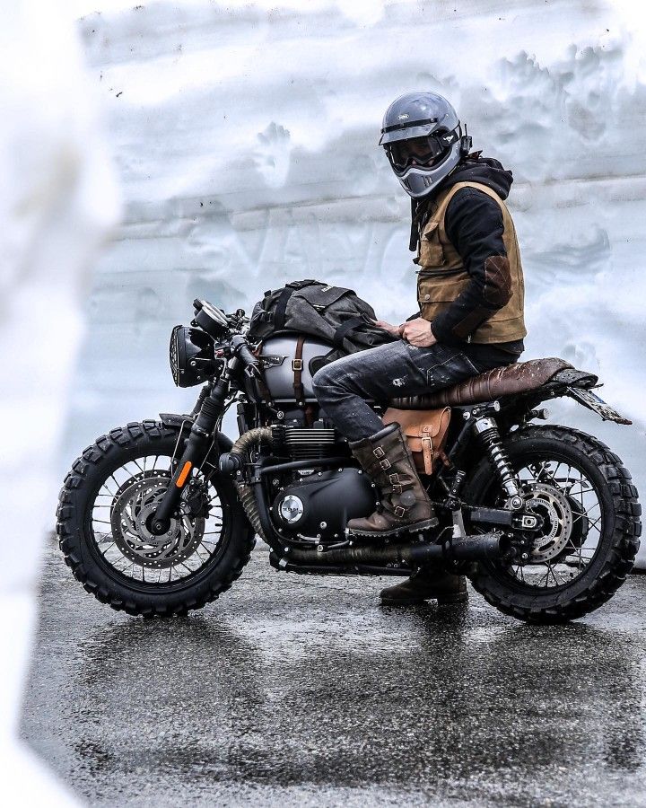 a man riding on the back of a motorcycle down a street next to snow covered ground