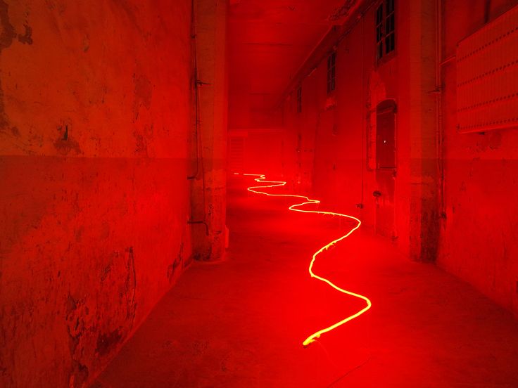 a long hallway with red light coming from the ceiling and on to the floor, there are no people in it