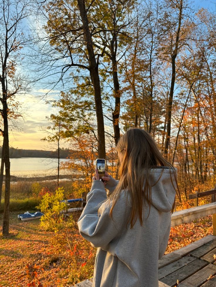 a woman taking a photo with her cell phone in the woods next to a lake