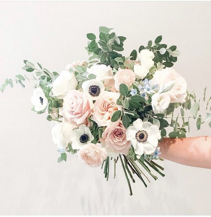 a person holding a bouquet of white and pink flowers with greenery in their hand