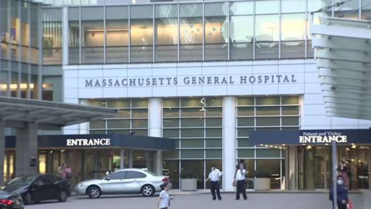 several people are walking in front of the masacustts general hospital building with cars parked outside