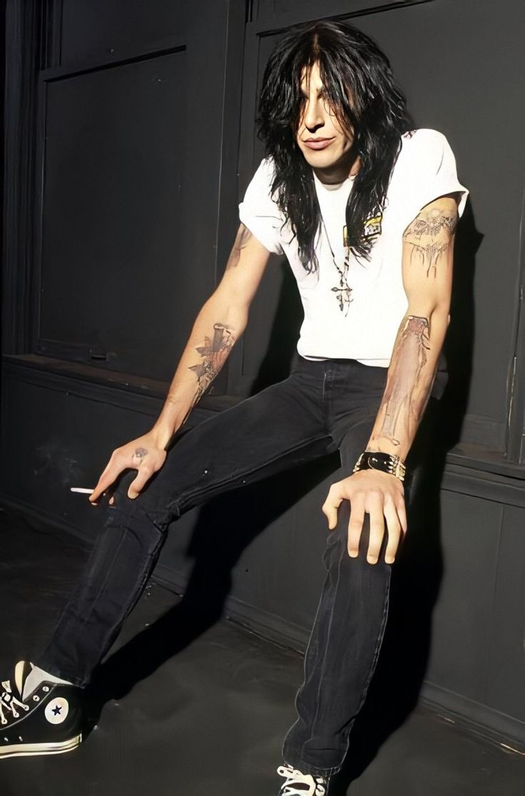 a man with long hair and piercings sitting on the ground in front of a black wall