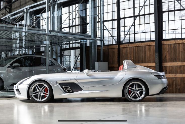 a silver sports car is parked in front of a large building with glass walls and windows