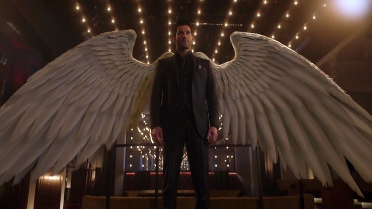 the man is standing in front of an angel's wings with lights behind him