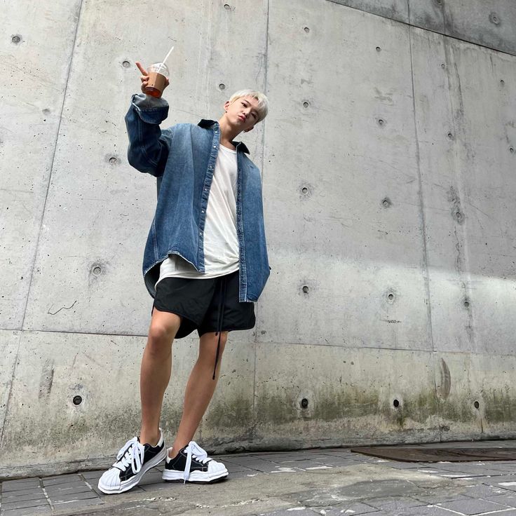 a young man standing in front of a concrete wall with his hand up to the sky