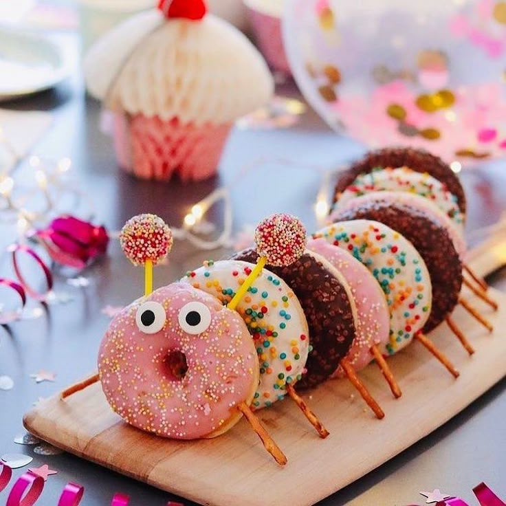 donuts with sprinkles and eyes are on a wooden board next to streamers