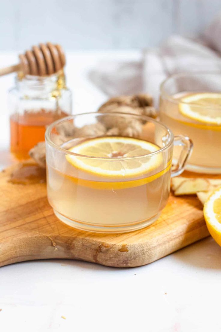 some lemons are sitting on a cutting board with honey and ginger in the background