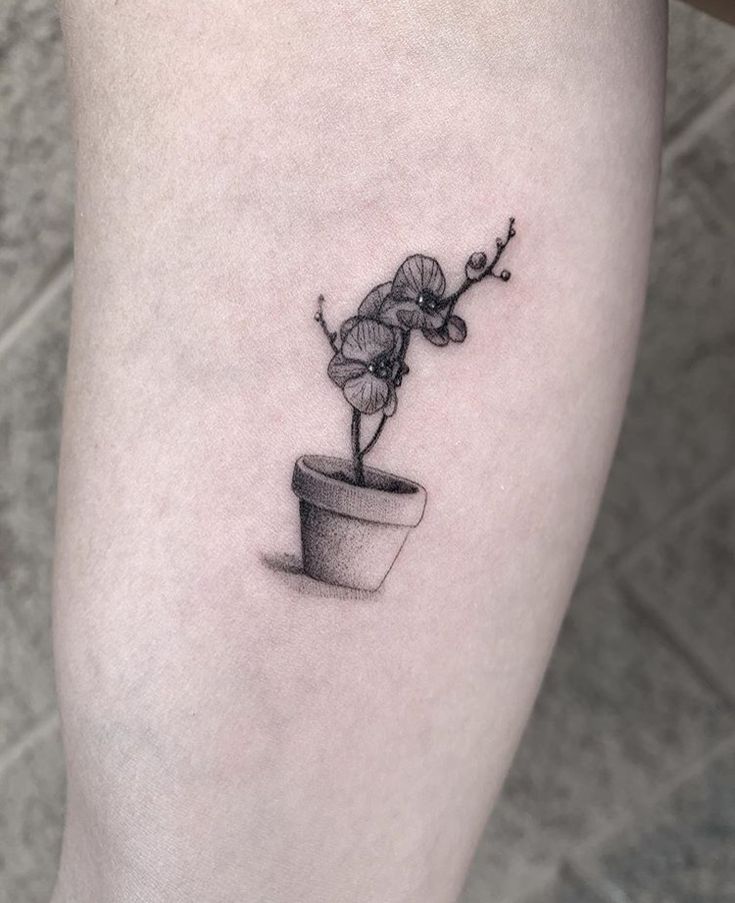 a black and white photo of a flower in a pot tattoo on the right thigh