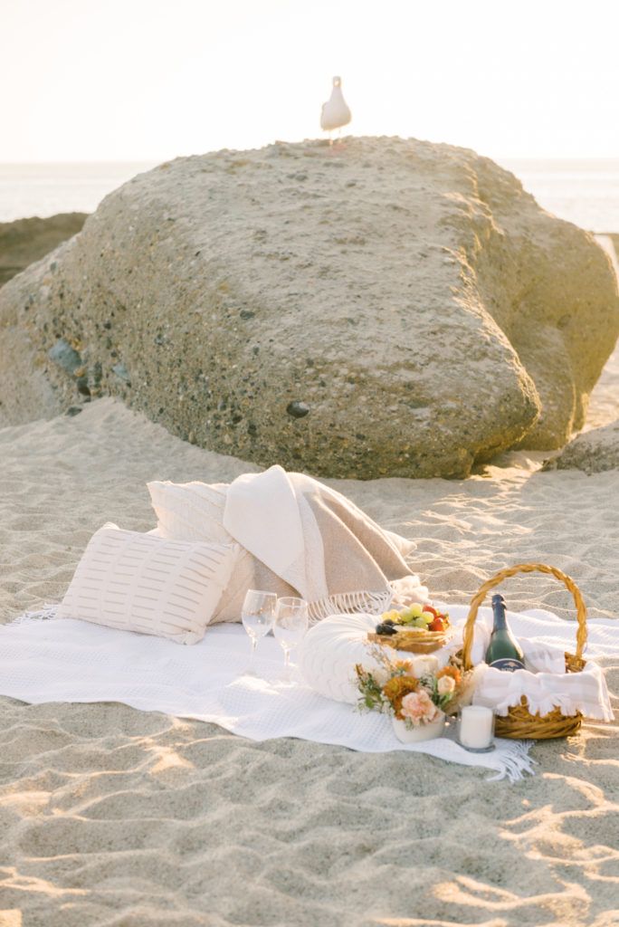 a picnic on the beach with an umbrella, food and wine in front of it