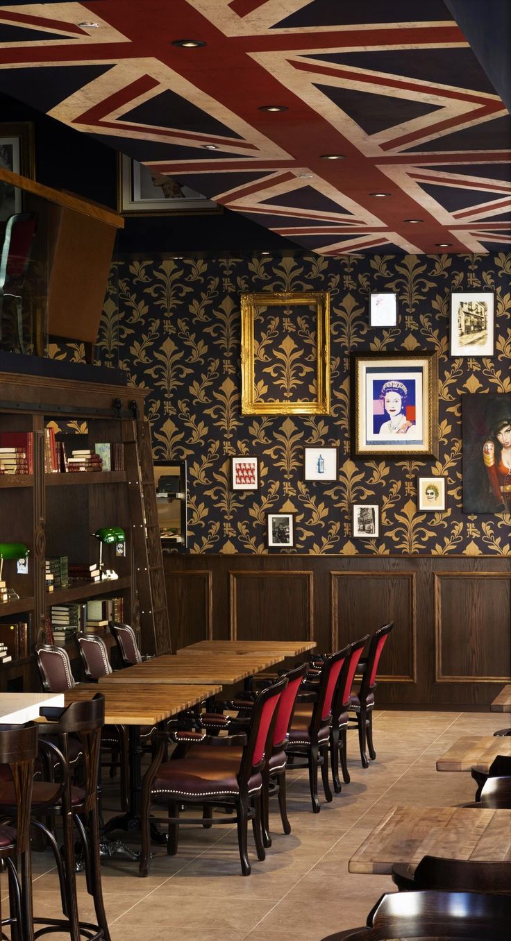 the interior of a restaurant with wooden tables and red chairs in front of an union jack wallpaper