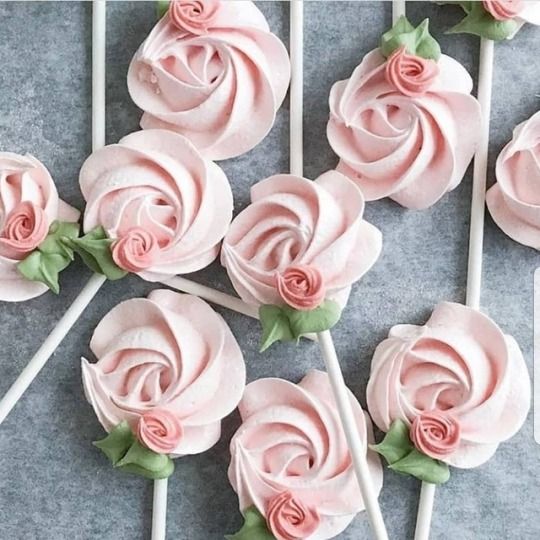 pink frosted roses are on top of white lollipops with green leaves