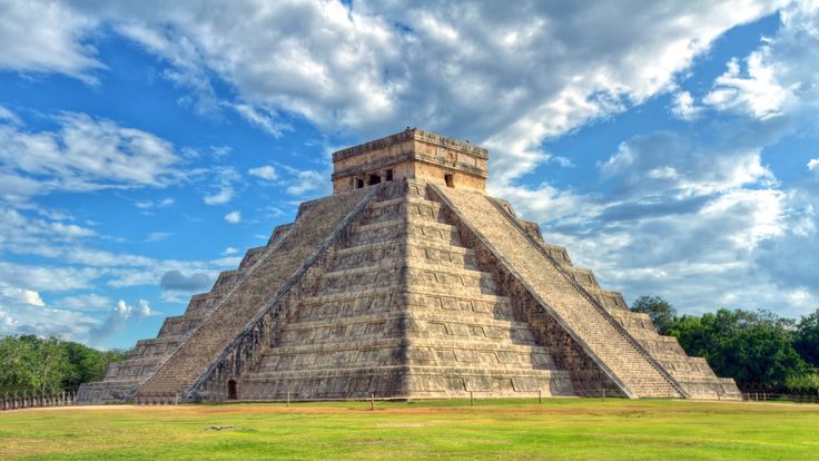 an ancient pyramid in the middle of a grassy field under a blue sky with clouds