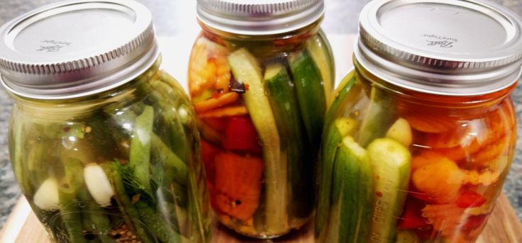 three mason jars filled with pickles and other vegetables