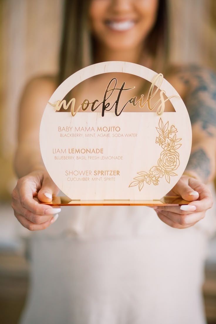 a woman in white dress holding up a wooden plaque with the word cocktail on it