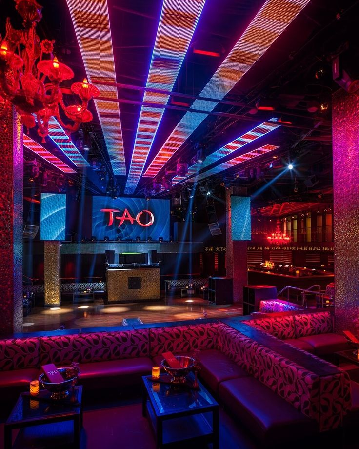 the inside of a nightclub with purple and red lighting on the ceiling, couches and tables