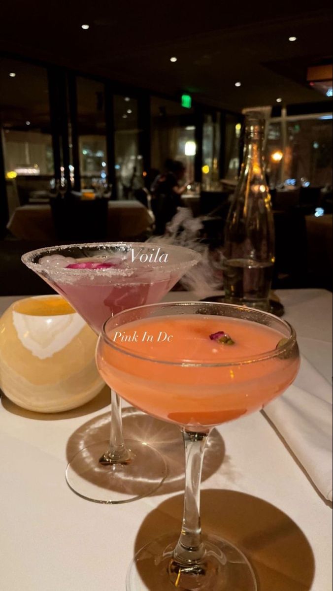 two cocktails sitting on top of a table next to each other in coupe glasses