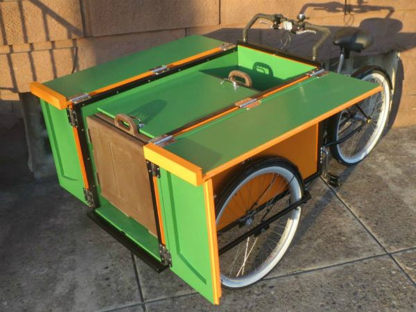 an orange and green bike with a sidecar attached to the front wheel, parked next to a brick wall