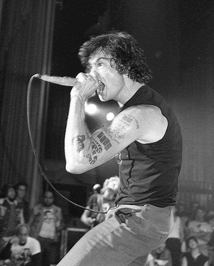 a black and white photo of a man with tattoos on his arm singing into a microphone