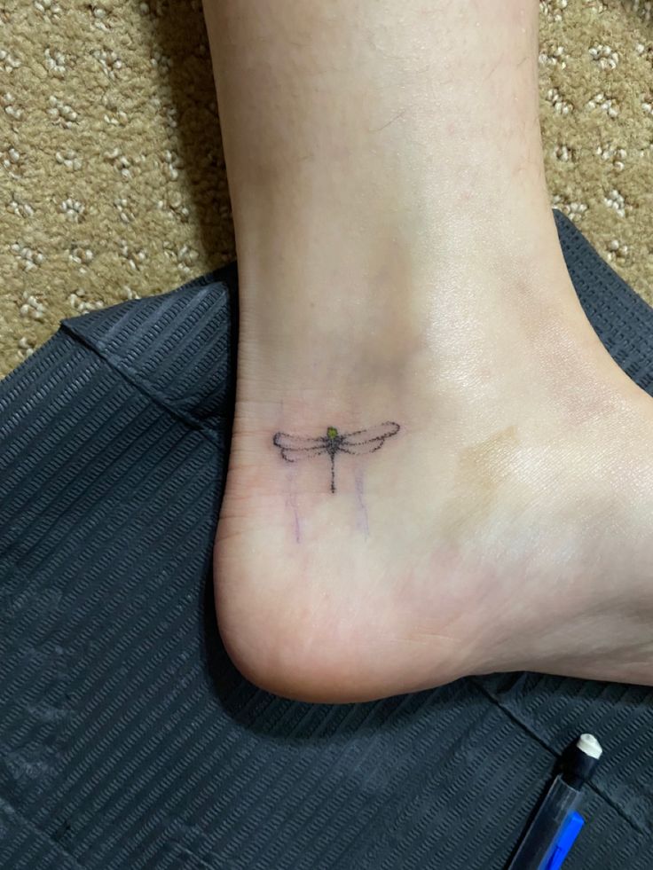 a small tattoo on the foot of a person with a dragonfly tattooed on it