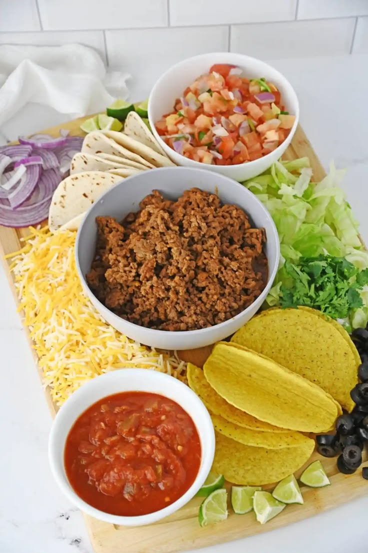 mexican food on a cutting board with salsa, tortilla chips and guacamole