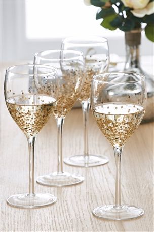 four wine glasses are lined up on a table with white flowers in the vase behind them